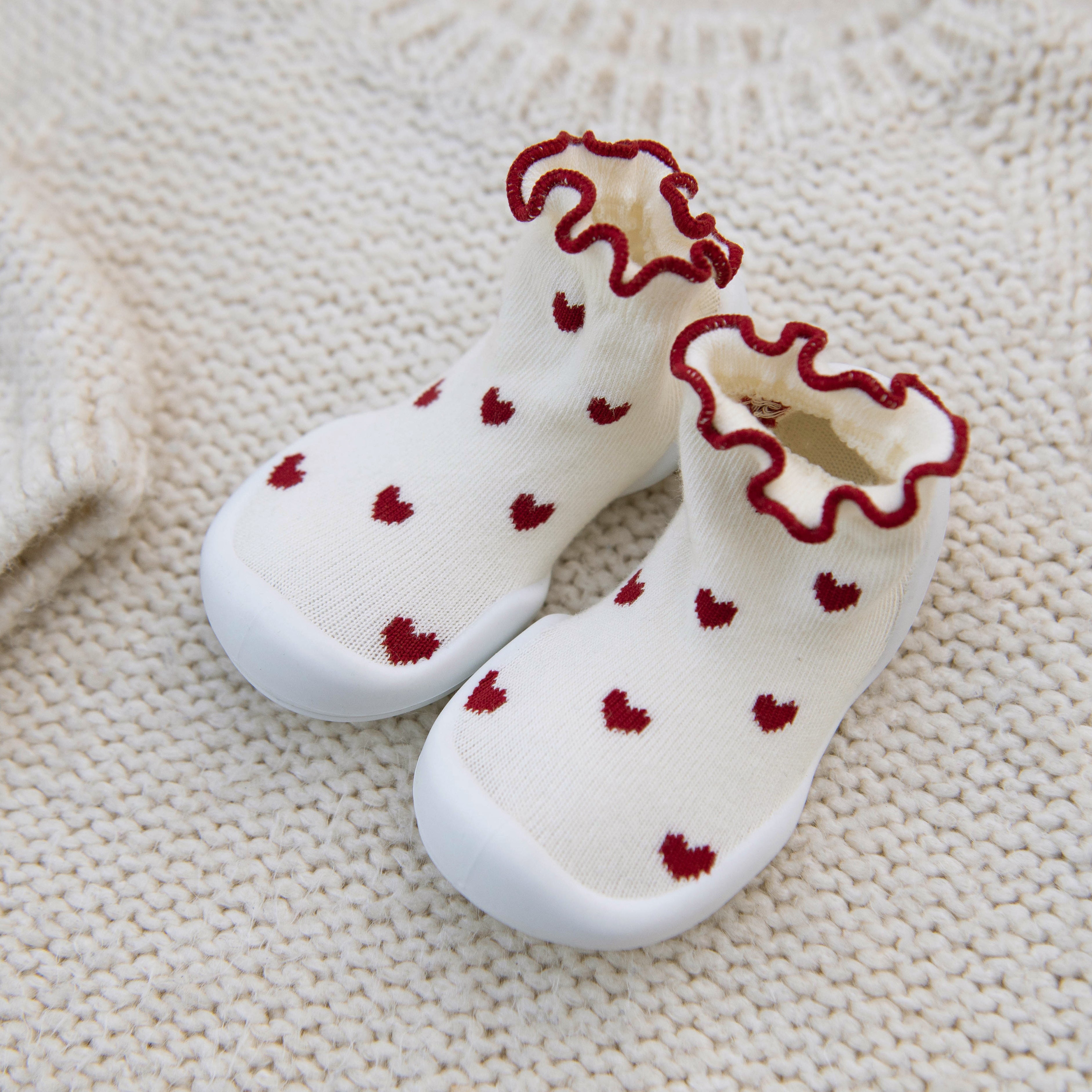Two white socks with red hearts and trim on a white knit sweater.