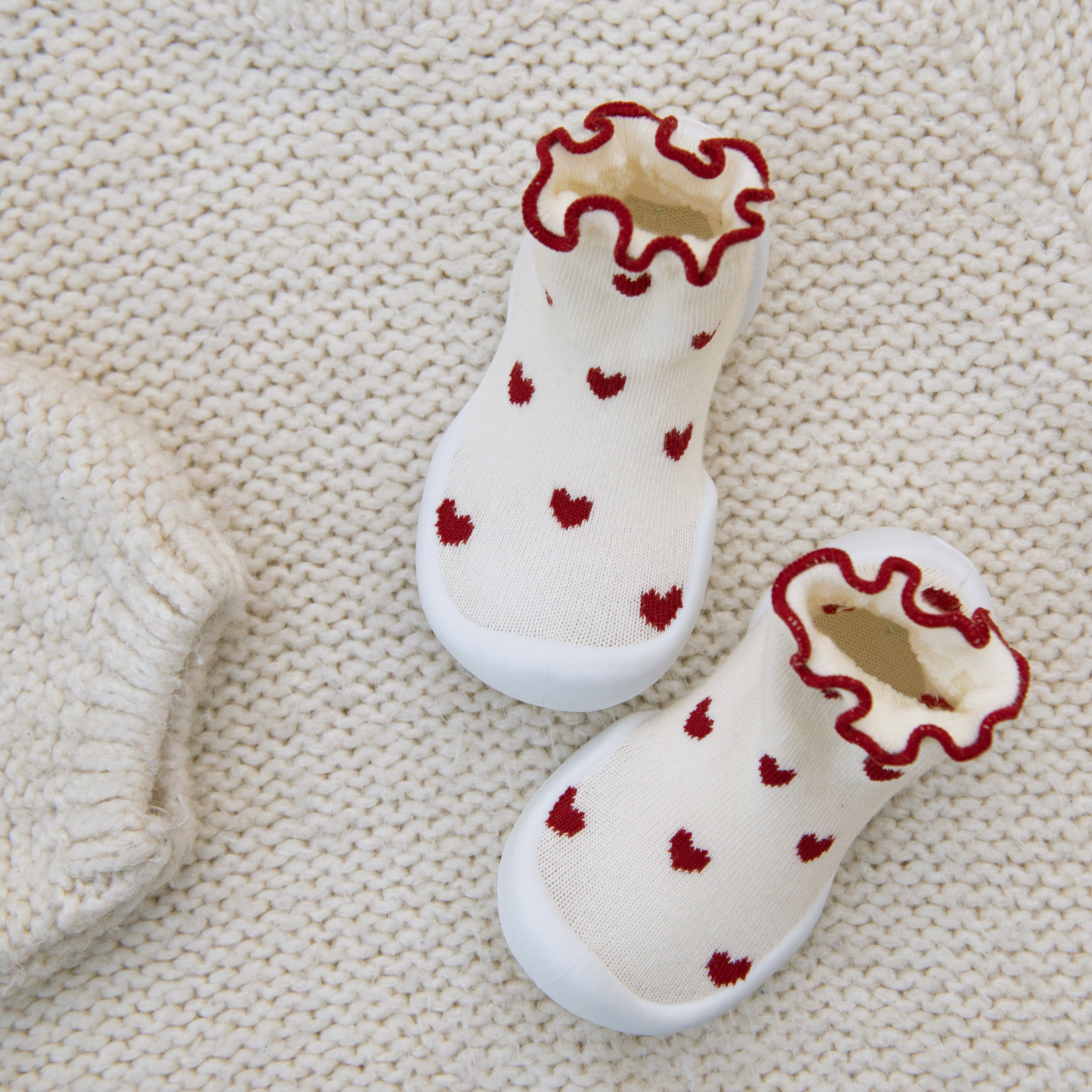 Two baby socks with red hearts on a white knit background.