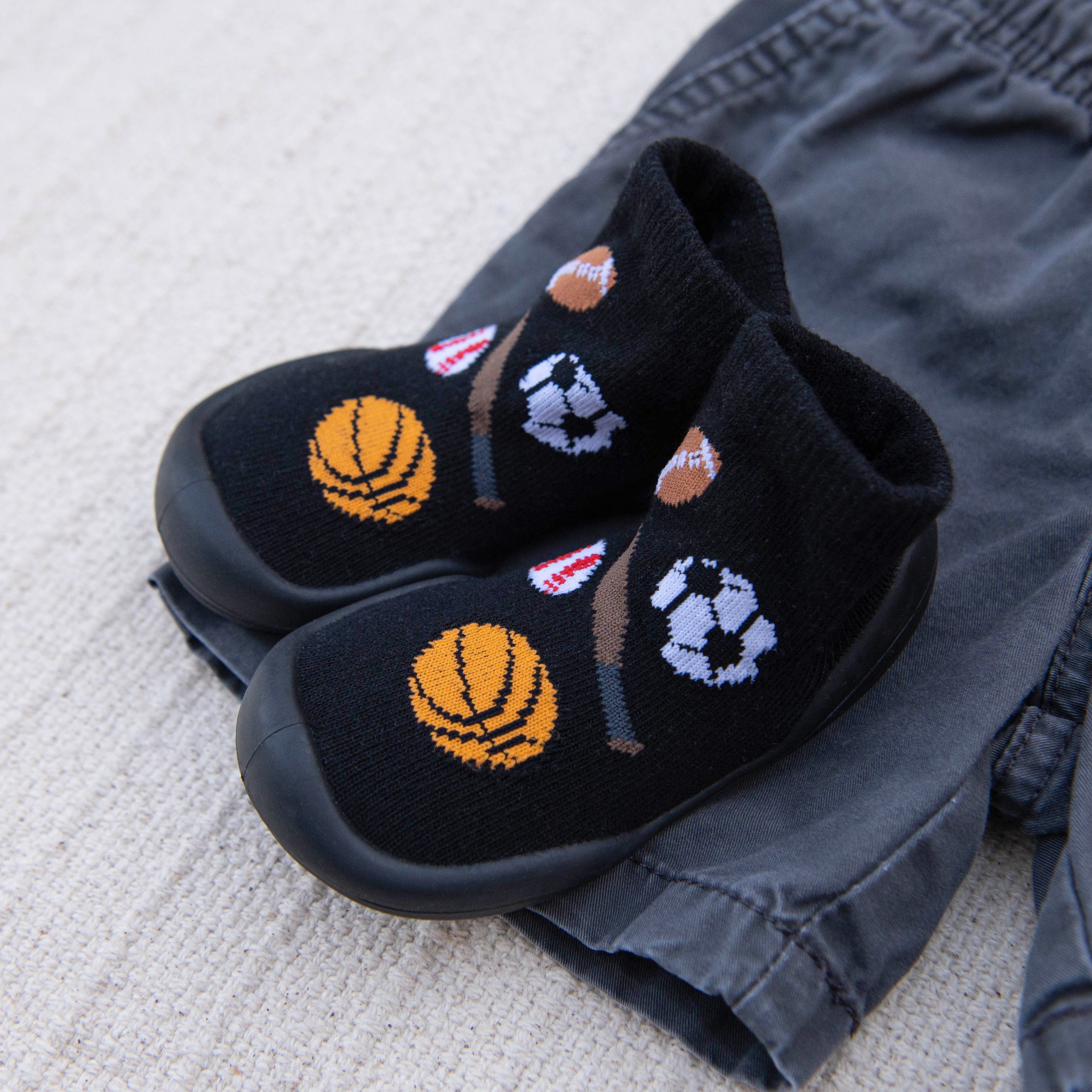 Black slipper socks with sports ball designs atop gray pants.