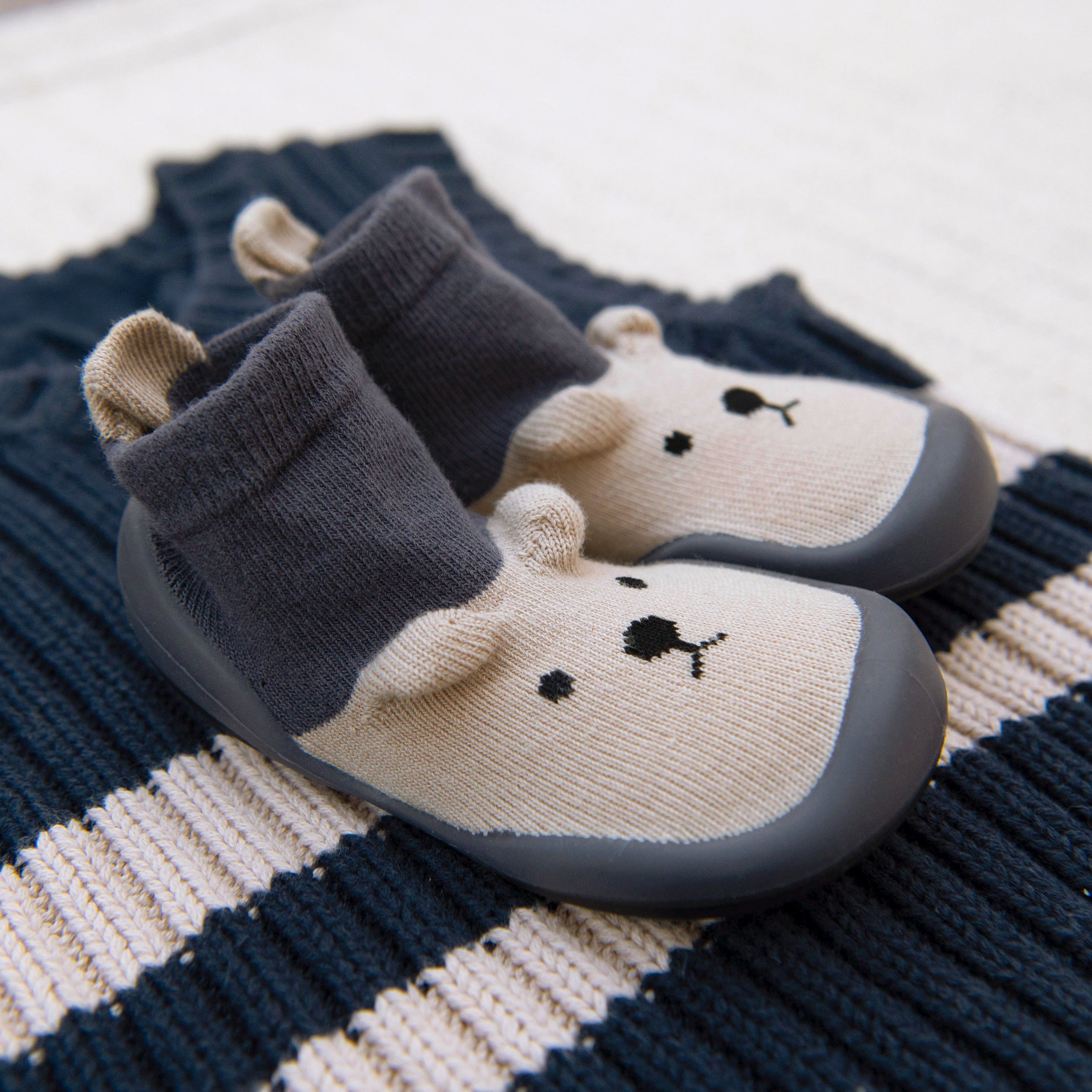 Pair of grey and white baby shoes with a bear face on a striped blue and white knit sweater.
