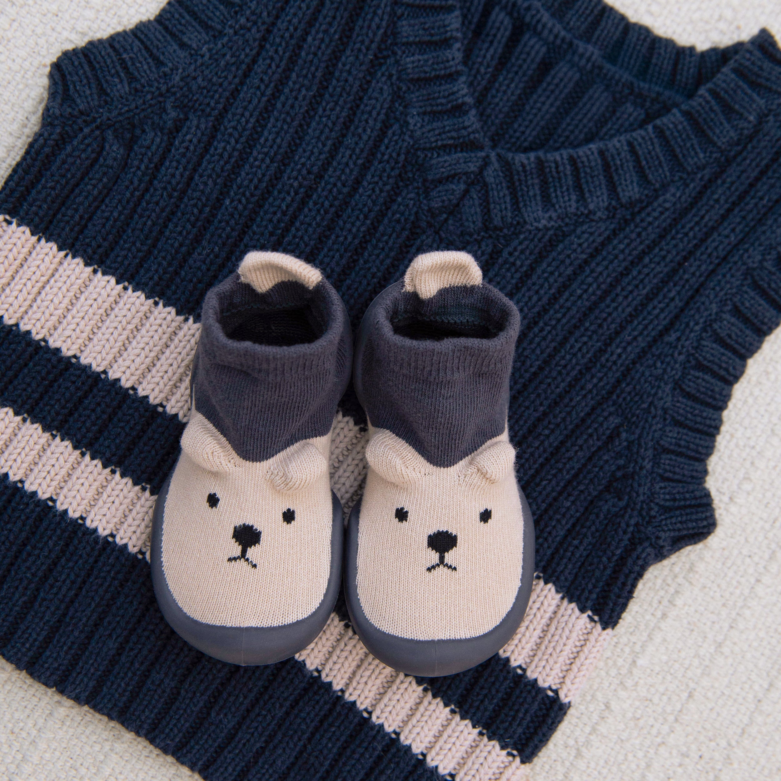 Baby bear slippers on a blue and cream knitted vest.