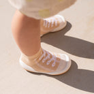 Baby wearing tan sock shoes with white design on concrete surface.