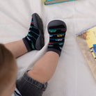 A baby wearing black socks with small colorful vehicles, and gray shoes.
