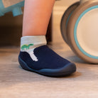Child's foot wearing blue sock-shoes with dinosaur design.
