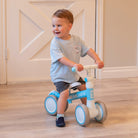 Toddler on a blue and white balance bike in a room.