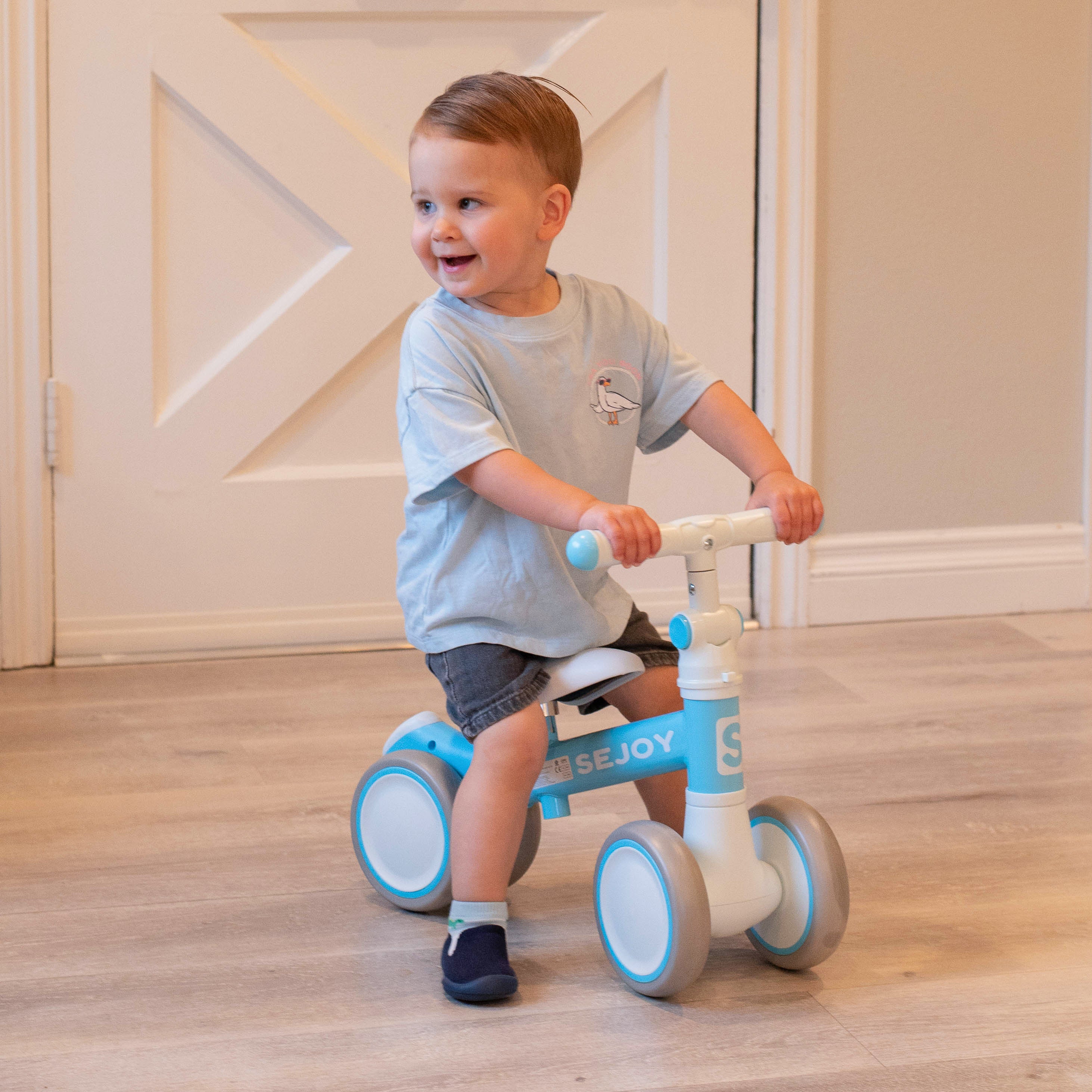 Toddler on a blue and white balance bike in a room.