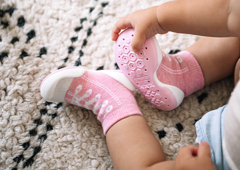 Baby wearing Komuello pink sneakers shoes with white soles on a textured carpet
