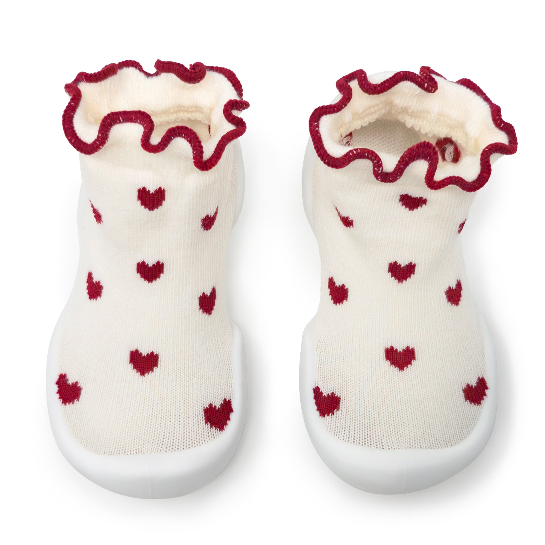 Pair of baby slipper socks, cream colored with red hearts and ruffled trim, white soles.