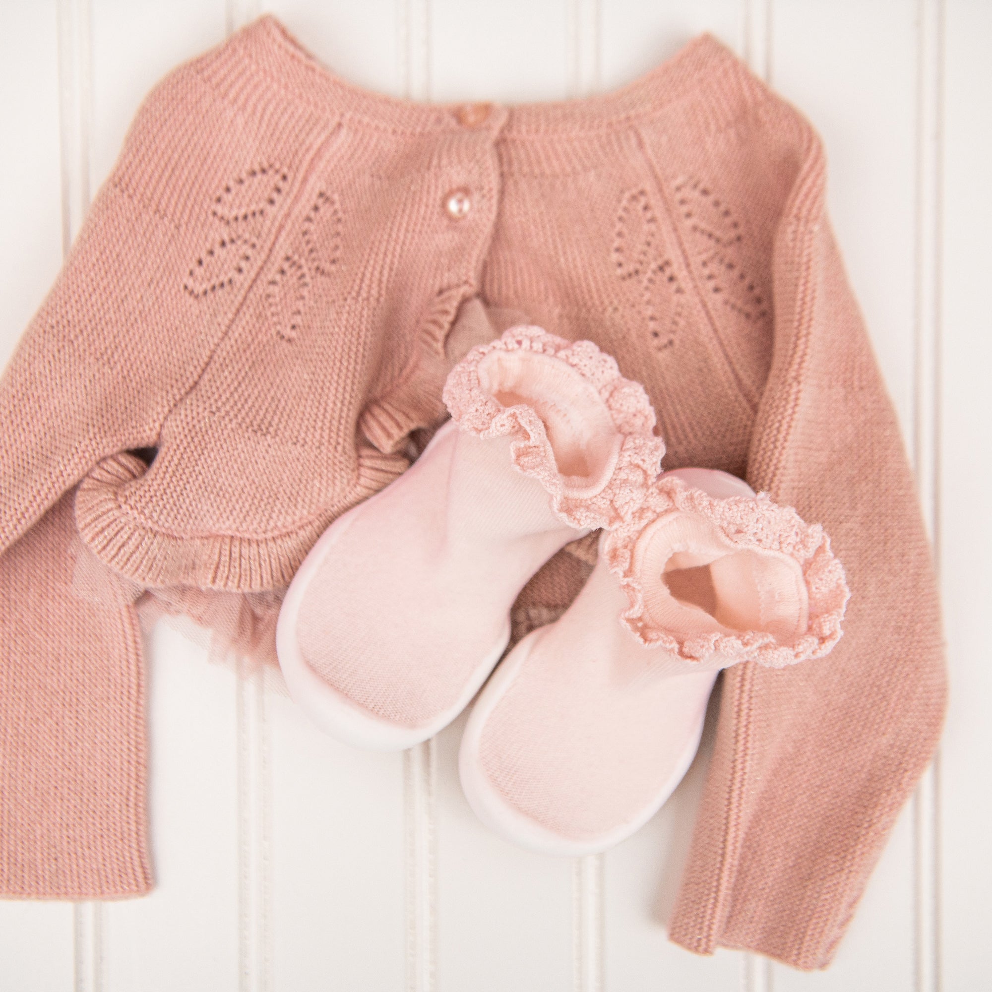 Pink knitted cardigan and baby shoes on a white wooden surface