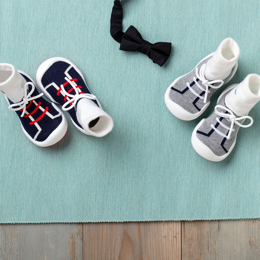 Two pairs of baby sock shoes and a bow tie on a blue-green textured surface.