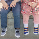 Two children sitting on a ledge, one wearing blue pants and grey shoes, the other wearing a pink dress and brown shoes.