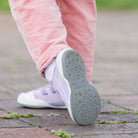 Close-up of child's pink corduroy pants, white socks, and lavender/white shoes with gray soles on brick surface.