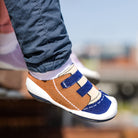 Close-up of a child's feet wearing blue jeans and brown, blue, and white striped slipper shoes.