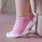 Close-up of a baby's feet wearing pink sock-shoes with white laces and soles.