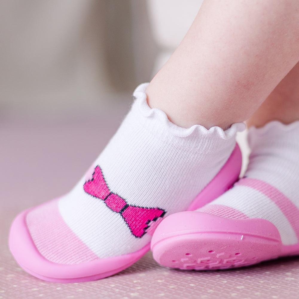 Baby feet in pink and white sock-shoes.