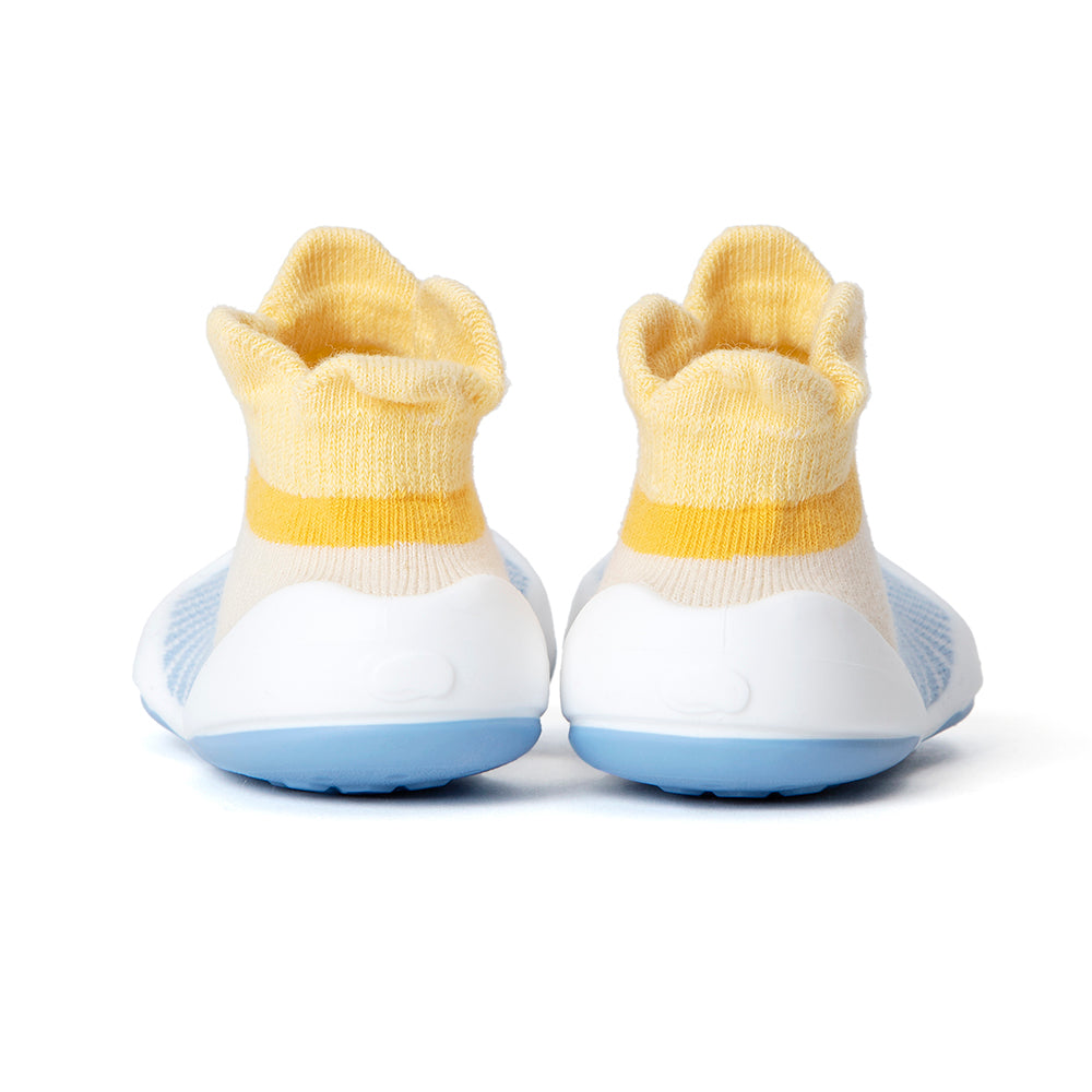 Back view of baby shoes with yellow sock-like uppers, white midsoles, and blue soles.