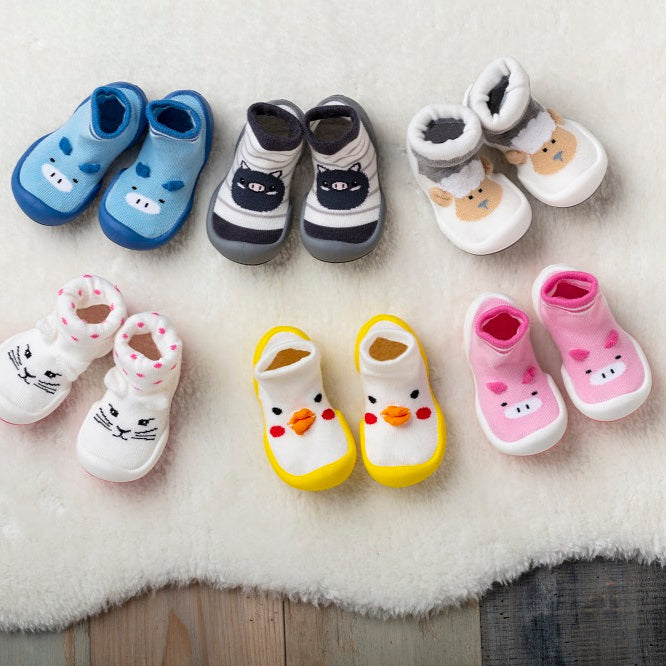 Various pairs of baby sock shoes with animal designs on a fluffy surface.