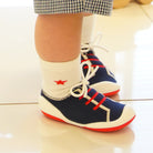 Child's legs in white socks with a red star, wearing blue and red shoes with white laces, under patterned shorts.