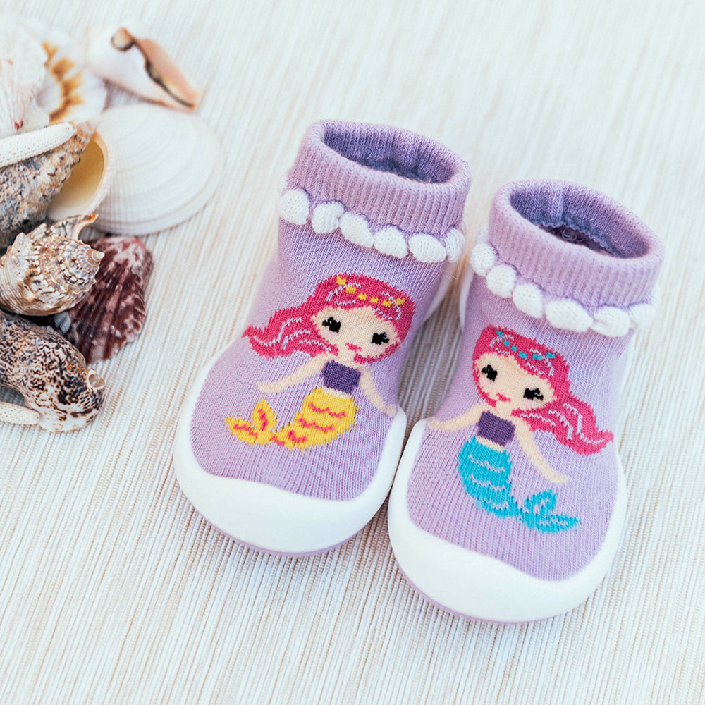 Pair of purple baby slipper shoes with mermaid design and seashell background.