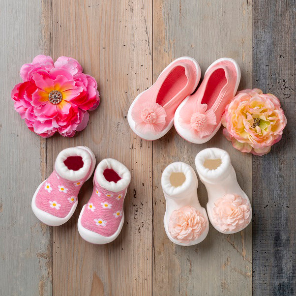 Four pairs of baby shoes with flower accents on a wooden surface.