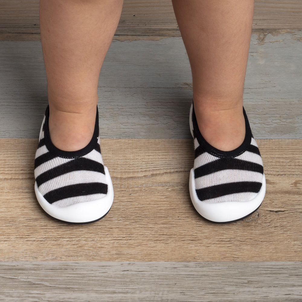 Child's legs wearing black and white striped shoes on a wood floor.