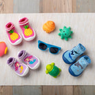 Overhead shot of toddler sock-shoes with summery designs, sunglasses, and toys.