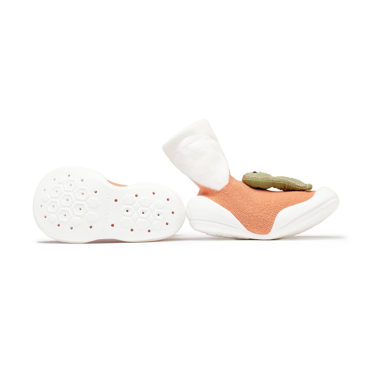 Two baby shoes with peach socks and a green alligator detail. The shoe on the left shows the sole of the shoe.