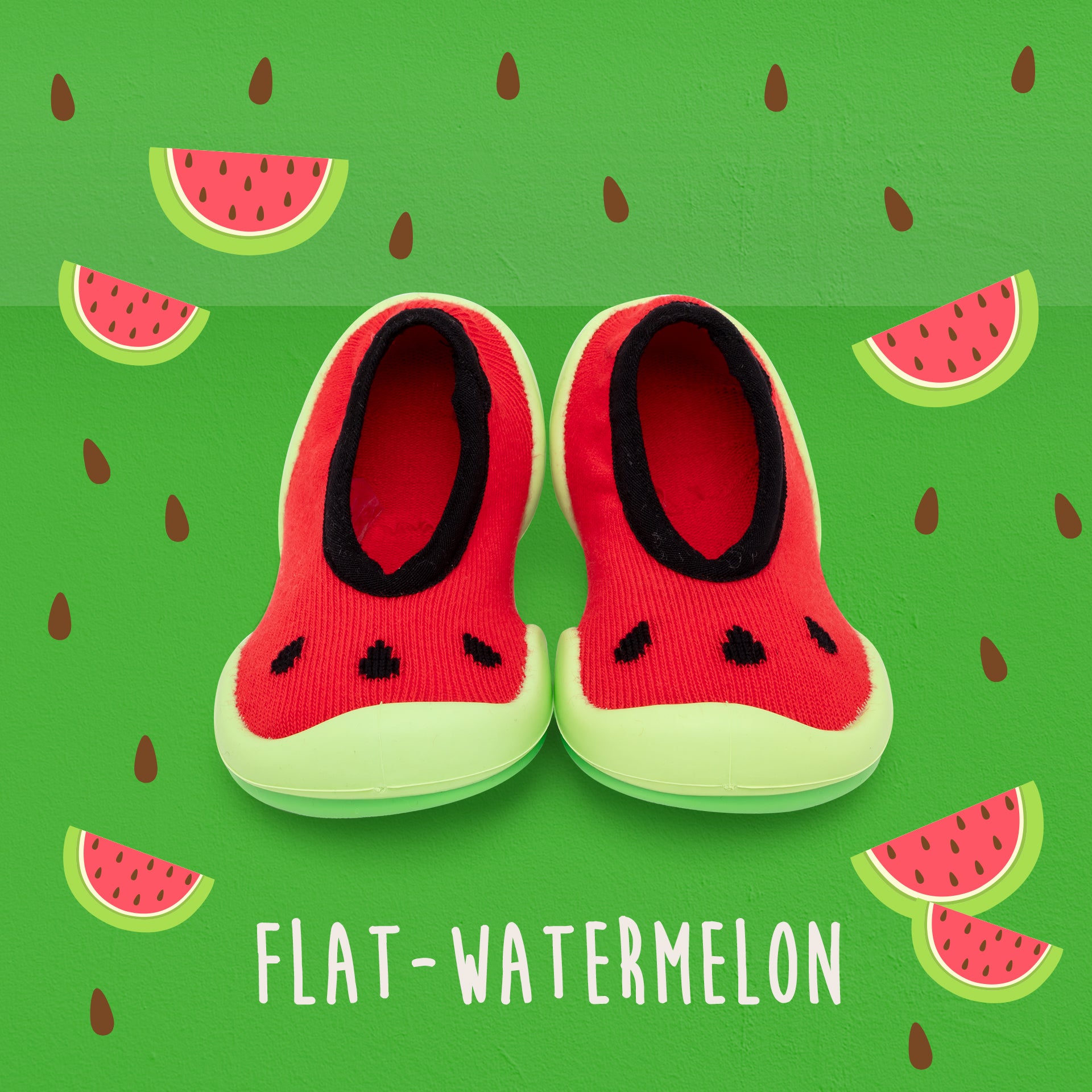 Two red and green watermelon-themed baby shoes on a green background with watermelon slices and seeds.