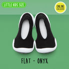A pair of black and white baby shoes on a green background.