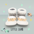 Two little lamb baby socks/shoes on a light blue background with star and lamb illustrations.