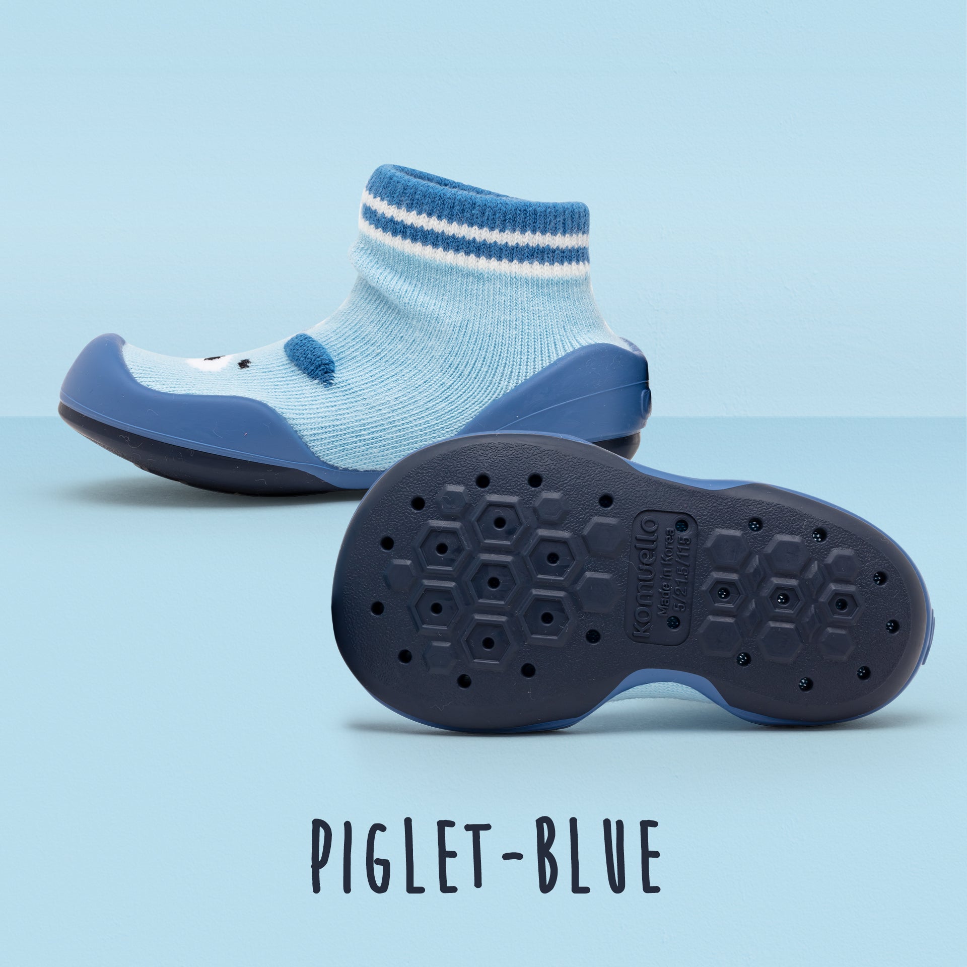 Two light blue baby shoes with sock-like tops and navy blue soles on a light blue background. One shoe is lying on its side exposing the bottom sole, while the other stands upright.