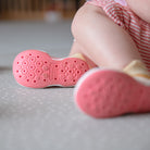 Close-up of baby shoes, pink soles with hexagonal grip pattern, sitting on a gray mat.