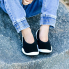 A child's legs and feet wearing jeans and black and white slip-on shoes.