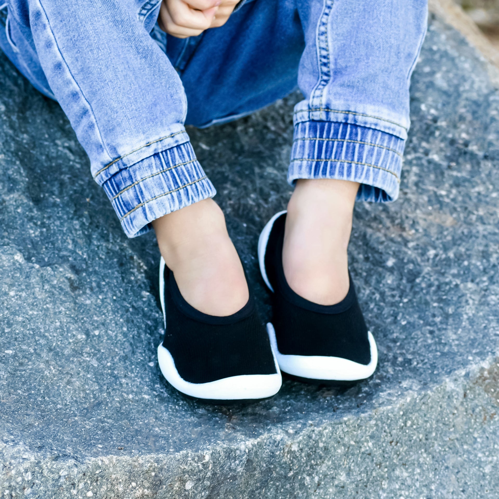A child's legs and feet wearing jeans and black and white slip-on shoes.