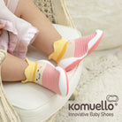 Baby wearing pink and white striped baby shoes with a yellow and cream trim.