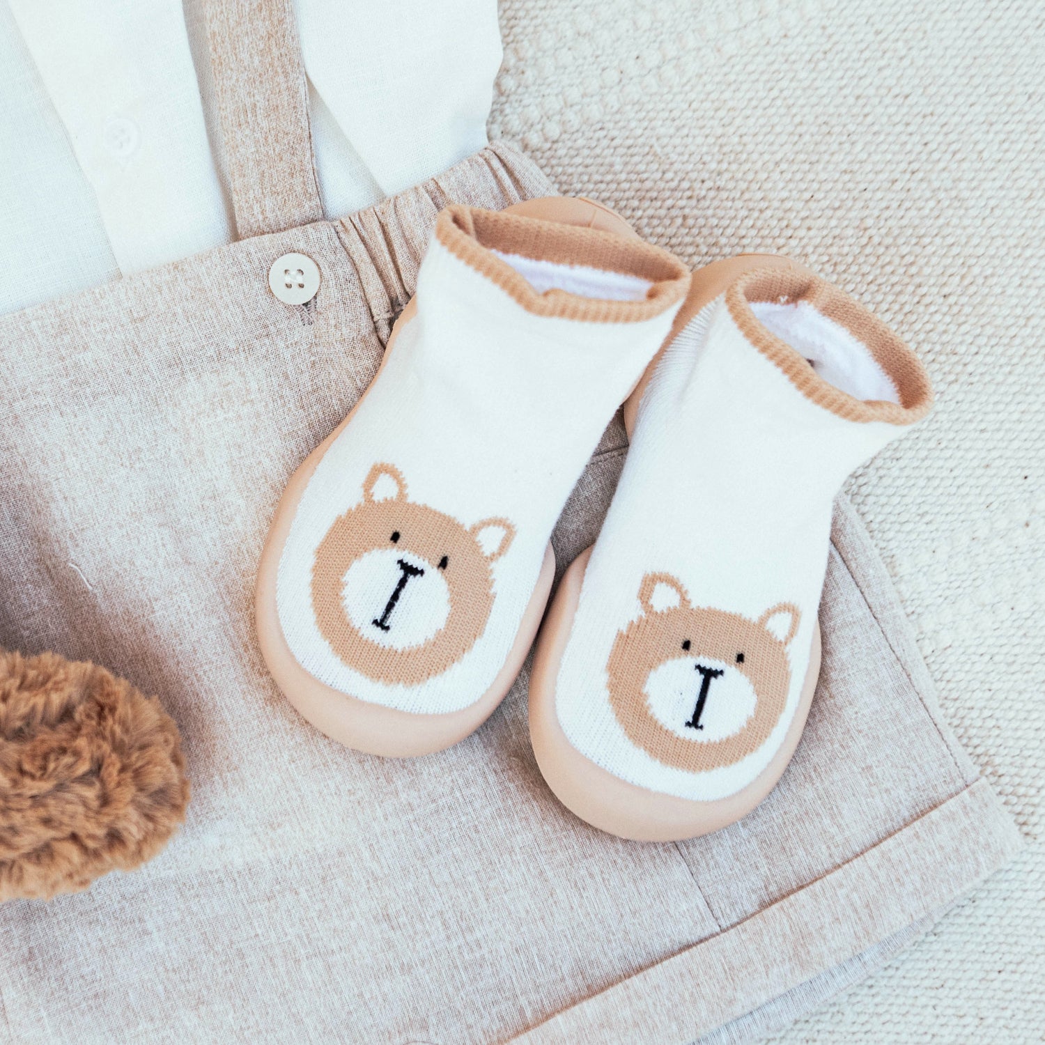 Two teddy bear baby socks and a beige romper.