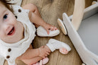 A baby sitting on a wooden floor wearing white shoes with floral accents.