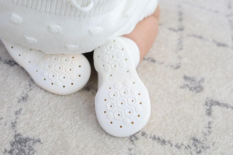 Close-up of a baby wearing white knitwear and non-slip booties on a carpet.