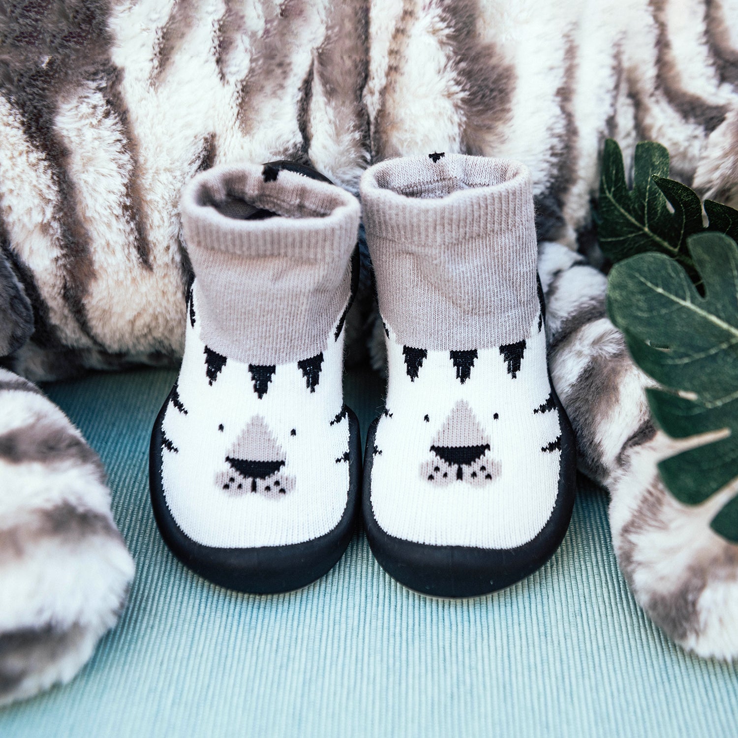 Two baby socks with a tiger face design, against a plush, striped backdrop.