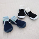 Two pairs of sock shoes, one blue and one black, on a beige fabric.