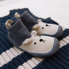Pair of grey and white baby shoes with a bear face on a striped blue and white knit sweater.