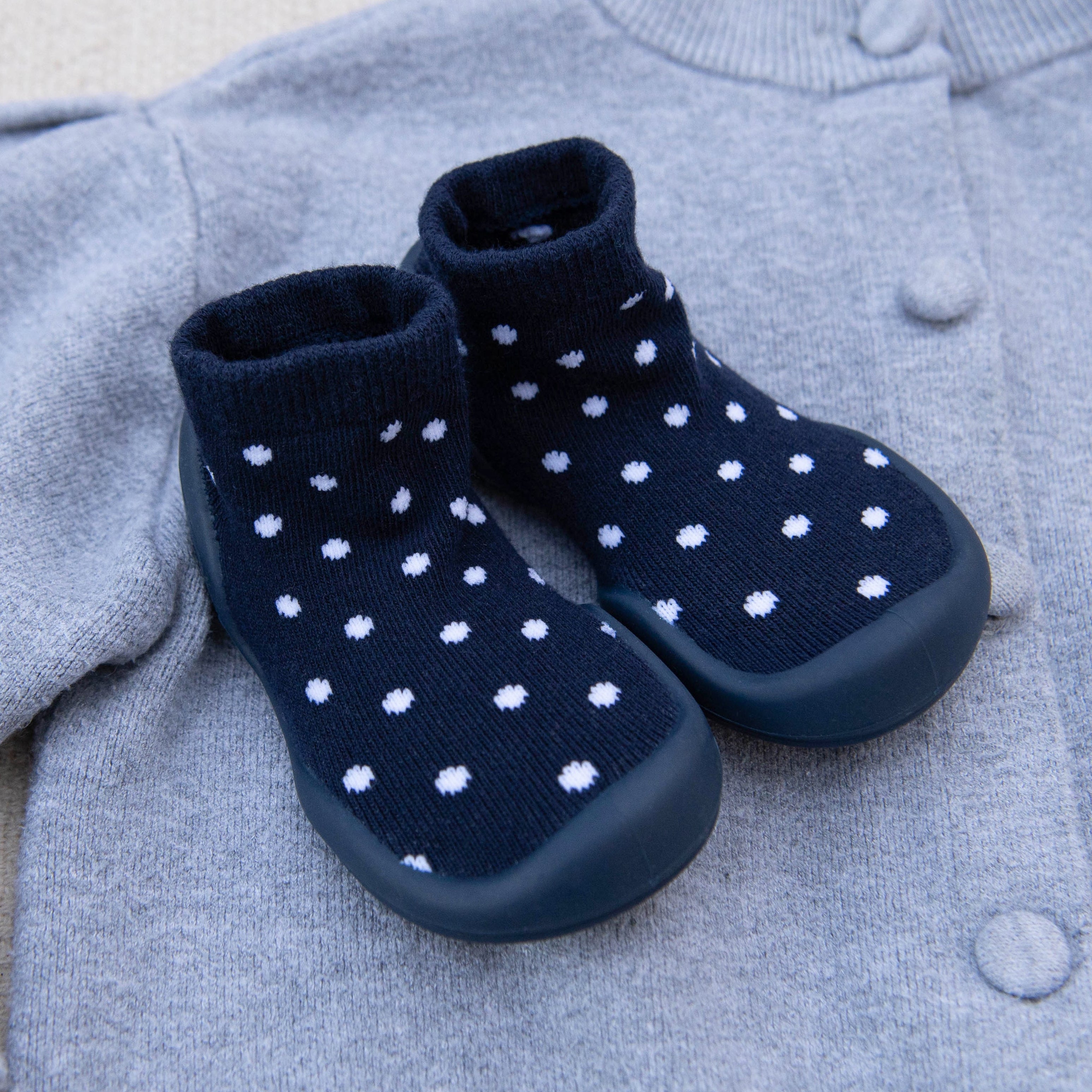 Two navy blue, polka-dotted sock shoes on a gray cardigan.
