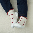 Baby wearing dark blue jeans, white socks with red hearts and trim, and white shoes on a soft, white, textured surface.
