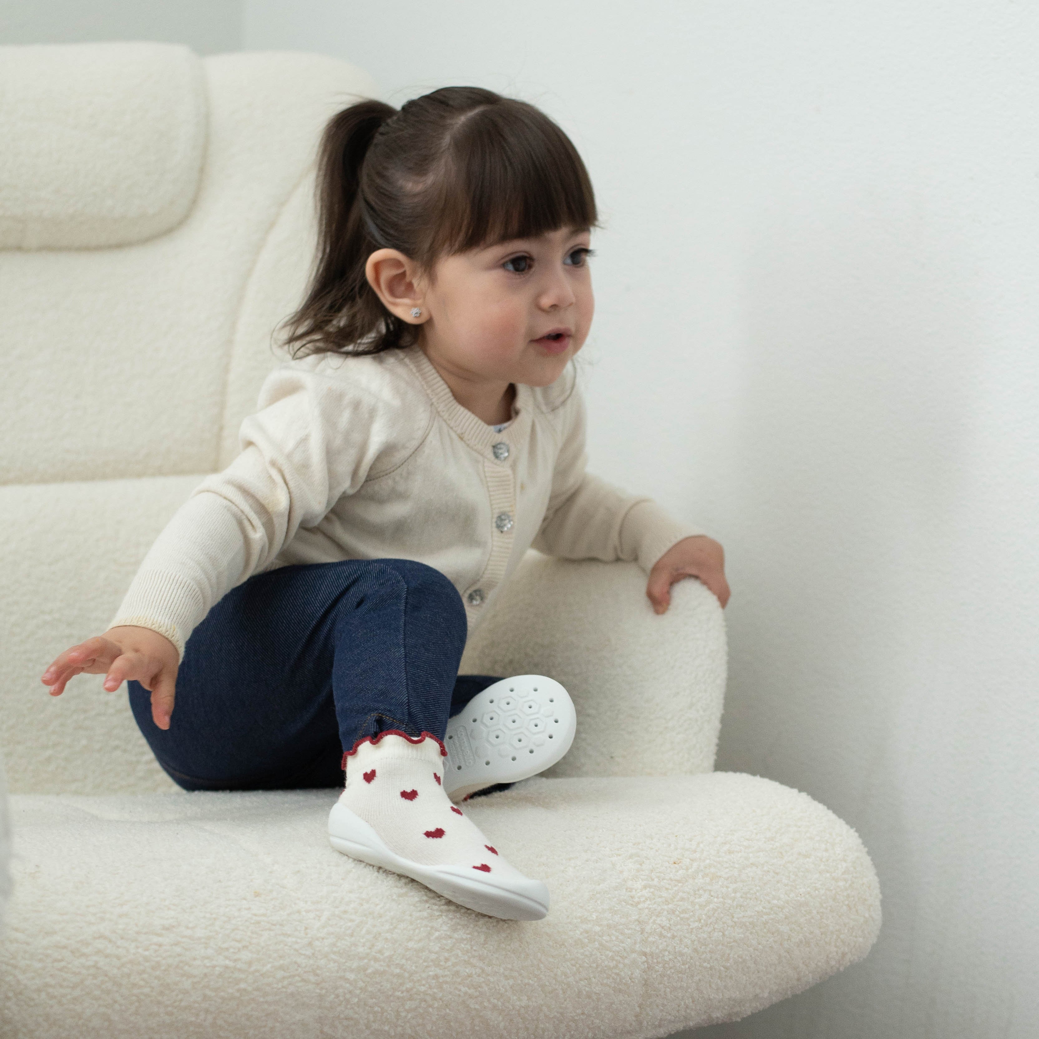 Child in chair wearing cardigan, jeans, and socks with heart pattern.