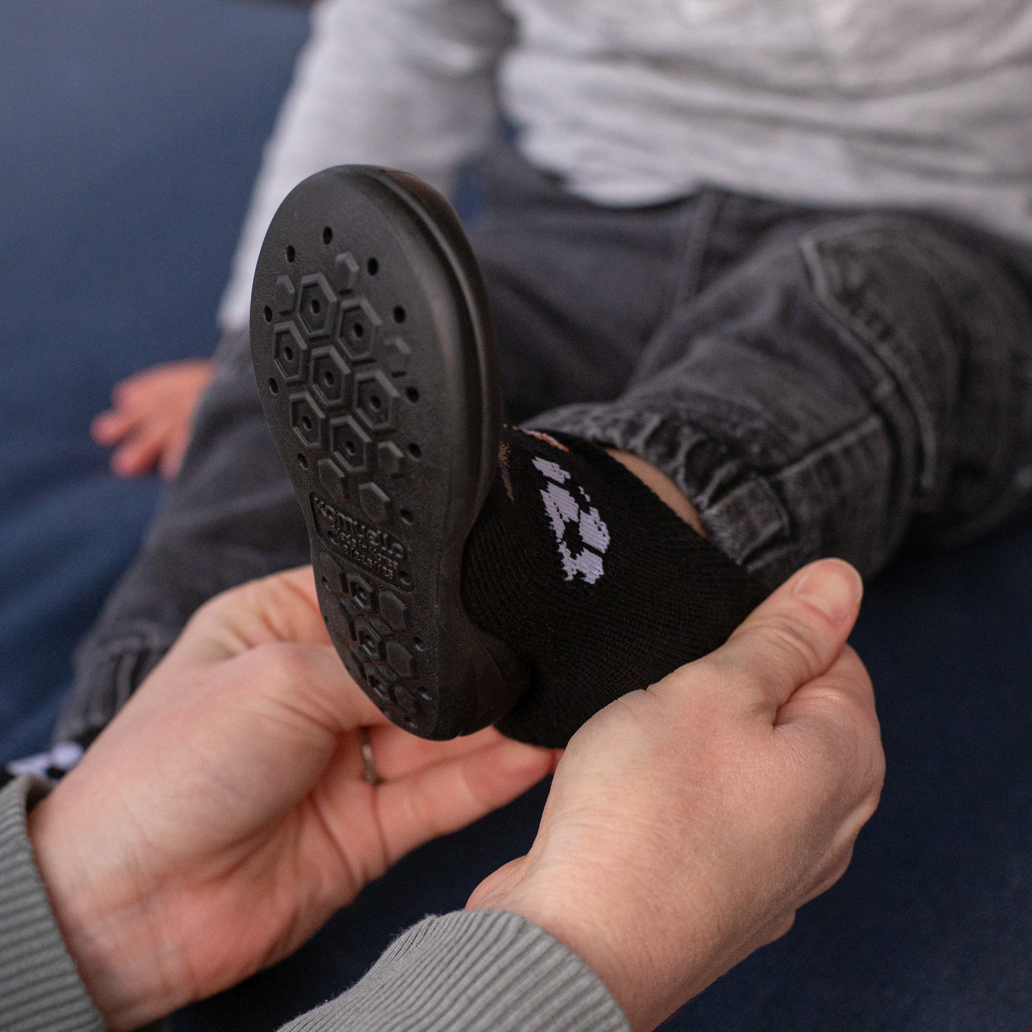 Child wearing a black sock and shoe, held up by hands.
