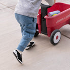 Toddler in gray shirt and blue cargo pants pulling a red Radio Flyer wagon.
