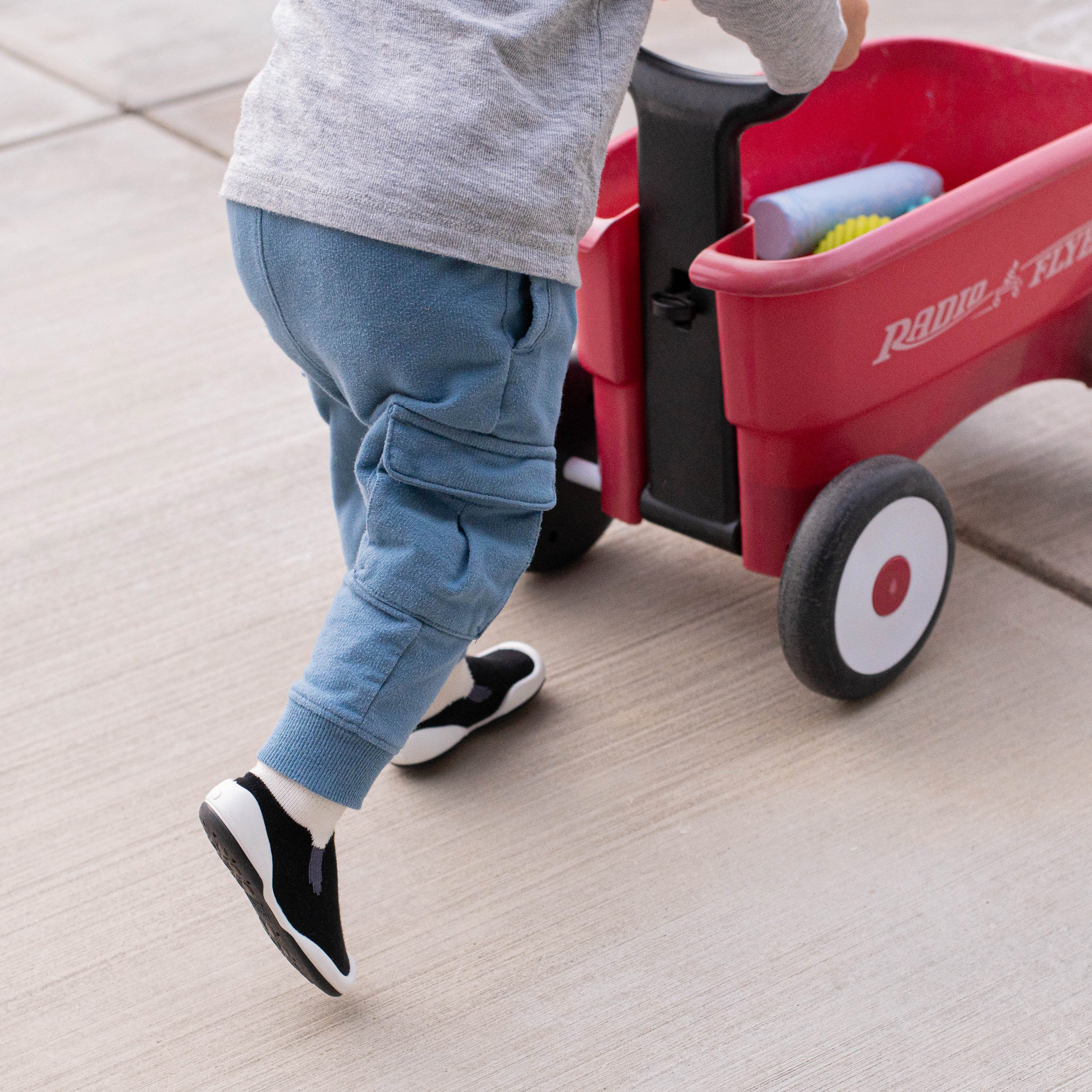 Toddler in gray shirt and blue cargo pants pulling a red Radio Flyer wagon.
