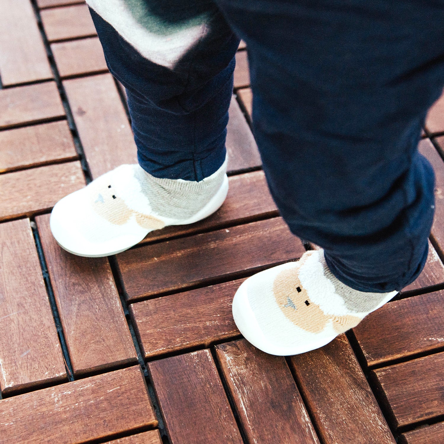 Child wearing Komuello grey little lamb sock shoes on a wooden floor.